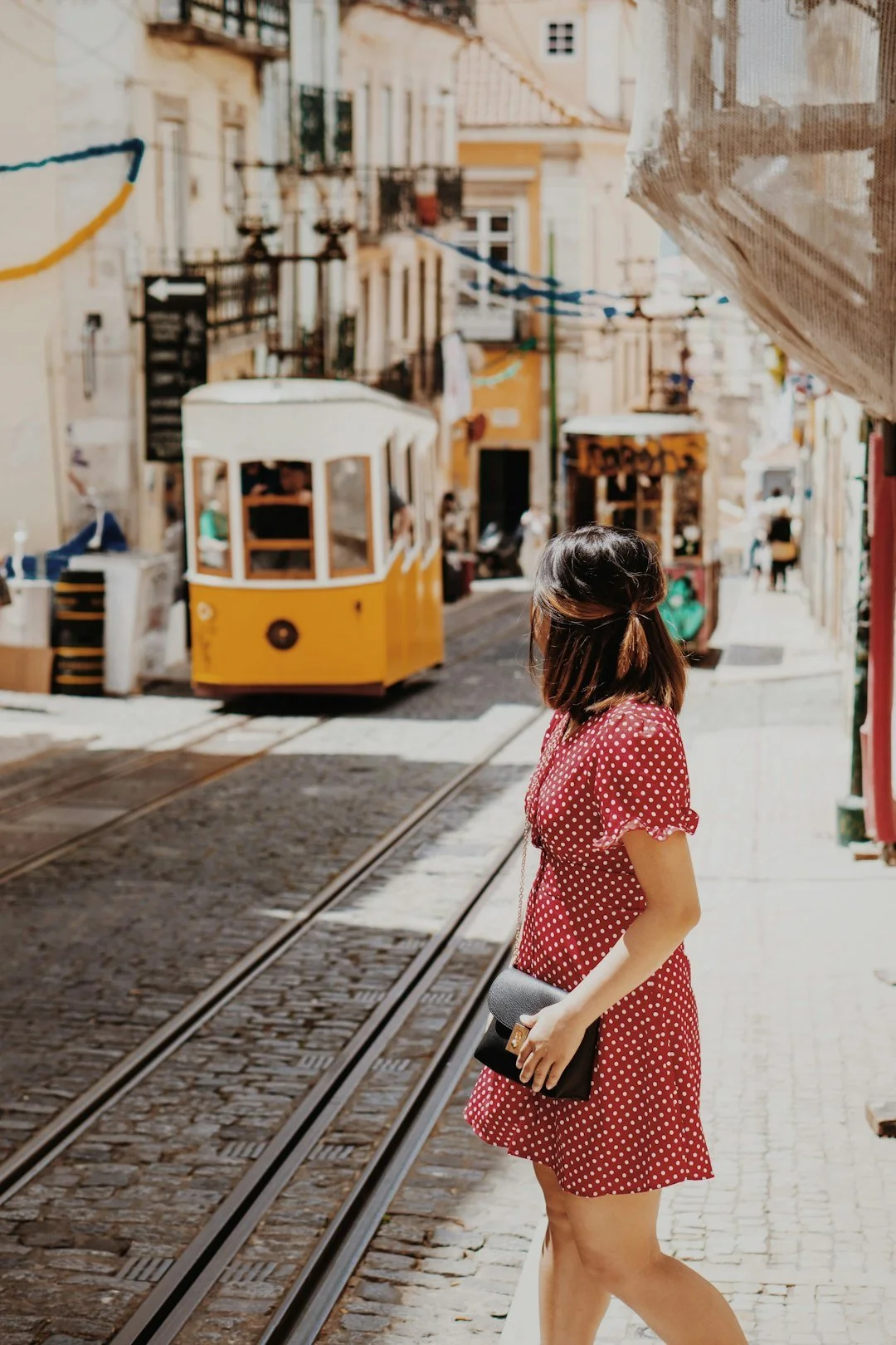 Woman exploring a sunlit Lisbon street with a yellow tram